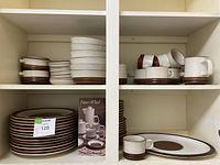 Multiple Denby Potters Wheel pieces on two cabinet shelves: bowls, plates, mugs and original pamphlet