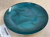 Top angled view of teal enamel plate showing surface design and condition with light scratches.