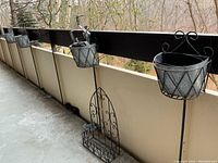 Overview of the set including 4 hanging balcony planters attached to balcony railing and one additional arched wrought iron planter on floor with base shelf.