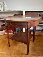 Full view of the round walnut end table showing top, drawer front and shelf with books in background.