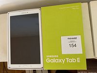 Samsung Galaxy Tab E tablet in white, displayed in box with the lid showing the product branding and specifications.