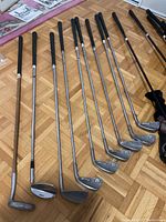 Photo showing nine golf clubs laid out with black grips and silver club heads, some marked with Ben Hogan logo.