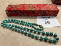 Turquoise beaded necklace arranged next to a decorative red fabric box for storage or display.