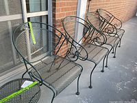 Four green wrought iron chairs aligned against brick wall