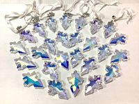 Photo showing an assortment of clear iridescent Swarovski crystal snowflake ornaments and partial pieces with white ribbons for hanging, laid out on a flat surface