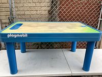 Wide angle view of large rectangular Playmobil kids activity table sitting on another white table. Blue plastic legs and molding with green recessed play surface. Playmobil logo along the side.