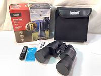 Photo showing boxed binoculars, carrying case, neck strap, lens cloth, and manuals laid out on table.
