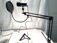 Full setup showing the boom arm with microphone mounted and pop filter in place, clamp visible on desk edge with possible rust.