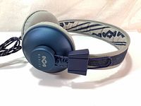 Photo of the wired on-ear headphones showing denim blue ear cup with logo, light gray ear pad, padded fabric headband with patterned inner lining, and attached braided wire.