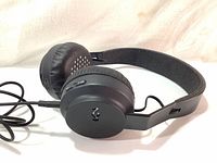 Black House of Marley Rise wireless on-ear headphones with cushioned ear pads and logo on ear cups, showing the side with audio cable attached.