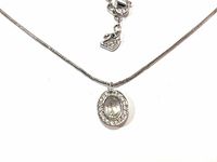 Close-up of the clear oval Swarovski crystal pendant with surrounding smaller crystals on a silver-tone chain, showing the swan logo charm on the clasp.