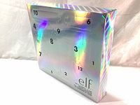 Holographic silver rectangular advent calendar box with 12 numbered doors in various shapes visible on front and side.