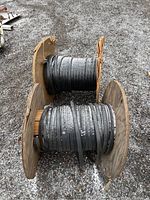 Two wooden spools of black flat cable resting on gravel, snow on cable.