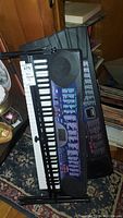 Two Casio electronic keyboards shown resting against a surface, one with a visible purple control panel and multiple buttons.