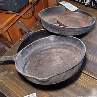Four cast iron pans arranged on a wooden surface showing heavy rust and scratches.