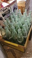 Photo of 24 green glass Coca Cola pint bottles inside weathered wooden crate
