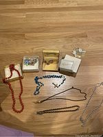 Full lot showing red and blue rosaries, pins in boxes, and multiple necklaces on wooden floor
