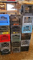 Stack of 16 assorted plastic crates of various colors and brands, showing wear.