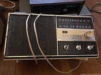 RCA Victor vintage radio with AM/FM dial, control knobs and fabric speaker cover showing wear, with audio cable
