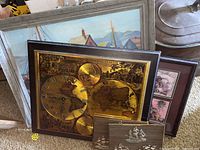 Photo showing framed seaside oil painting behind golden world map clock and framed teddy bear prints beside Columbus ship plaques.