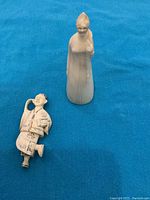 Both figurines on blue fabric background, small bone figure at left, tall bisque porcelain figure at right