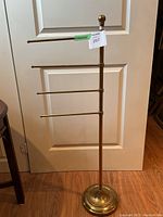 Front view of the full brass towel rack showing all four arms extended horizontally with round weighted base and vertical pole with finial top.