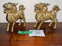 Front view of both solid brass Chinese dragon statues placed side by side on a wooden surface with a measuring note showing height and length.