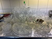 Wide view showing multiple glass and crystal serving bowls, platters, decanter, and decorative pieces with intricate cut patterns and clear glass surfaces.