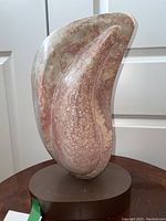 Front view of carved stone sculpture with wood base, mottled pink and green marble on brown oval base
