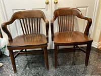 Front view of two solid wood desk chairs side by side, showing curved arms and slat backs