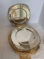 Stack of silver-plated charger plates with one leaning to show ornate scrollwork border and reflective surface