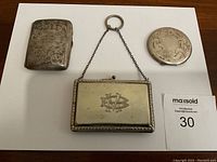 Three items displayed on white background: rectangular case, round compact, and rectangular minaudiere purse