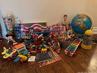 Overview of lot showing assortment of toys on floor including pull-toys, toy cars, boxes, books and globe