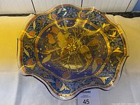 Top view of glass dish showing blue, burgundy, and gold intricate patterns with floral and geometric shapes.