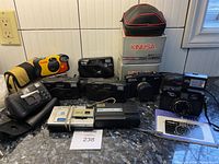 Photo showing multiple vintage cameras including Kodak disposable cameras, two Kinusa cameras, Konica camera, Victor camera, Minolta Freedom 200, and Yashica ME1 with flash in the background.