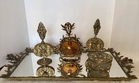 Front view of mirrored vanity tray with acanthus leaf border, three perfume decanters and cache pot arranged on tray