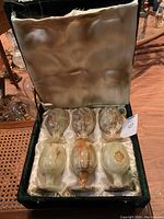 Six green onyx stone wine glasses in original velvet-lined satin box, showing natural variegated coloring and box wear.