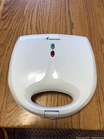 Top view of closed white Toastmaster waffle maker with power and ready indicator lights.