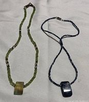 Photo showing the two beaded chokers laid flat on a light background, clearly displaying the beads and rectangular pendants.