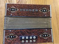 Close front view of the accordion showing brown marbled finish, decorative details, buttons, and HOHNER branding.