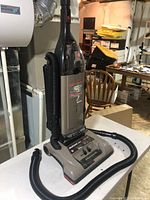 Photo of grey Hoover WindTunnel upright vacuum with clear dirt collection bin and black hose accessory in basement setting