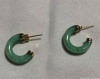 Close-up photo of pair of small curved jade hoop earrings with gold-tone metal posts and caps.