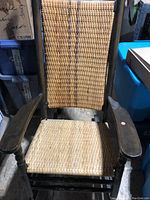 Front view of the wicker rocking chair showing woven seat, backrest, and wooden armrests with dark wood finish.