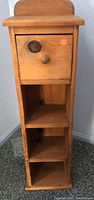 Front view of wood knick knack stand showing one drawer with knob and three open shelves below.
