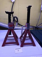 Photo of two red car jack stands side by side on a flat surface with labels.