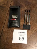 Three silver-colored nickel tungsten slim darts in a black RTO branded case on a brown wooden surface