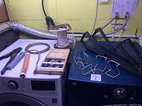 Overview of assorted hardware tools and accessories on top of appliances, including coils, pliers, a wire spool, saw blades and metal hooks.