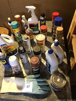 Top view showing various household chemical cans and bottles including insecticide, lubricant, rust protector, and cleaning agents along with rubber gloves.