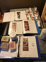 Photo showing two binders with pages of instructions and pictures for makeup application and supplies, several blocks of modelling clay and a container of rubber compound on a white surface.