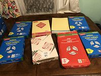 Photo showing 6 unopened reams of Staples multiuse copier paper (5 blue packs), 1 red pack of copy paper, 2 yellow legal pads and a box of Staples printer paper.